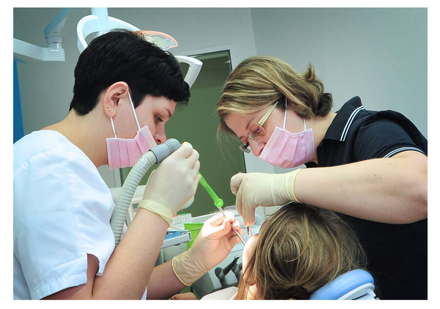 Zwei Zahnärztinnen tragen Mundschutzmasken und behandeln einen Patienten. den man nicht sieht