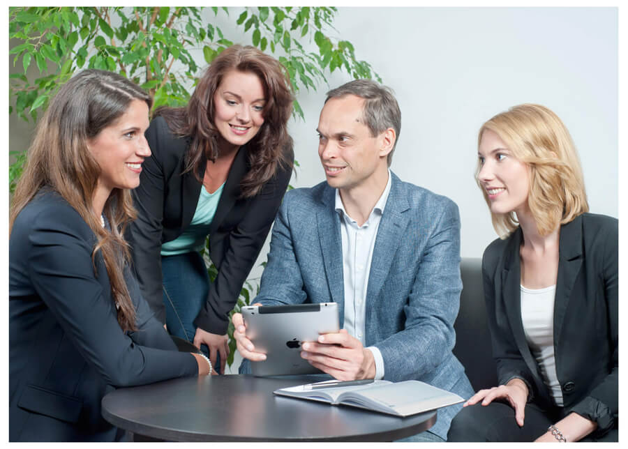 Firmenshooting stellt dar eine Gruppe von Geschäftspersonen, darunter der Geschäftsführer, sitzt um einen Tisch herum und betrachtet ein Tablet, Sprechsituation oder Beratung