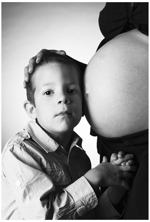 Babybauch München ein Junge schmiegt sich an den grossen Bauch der schwangeren Frau