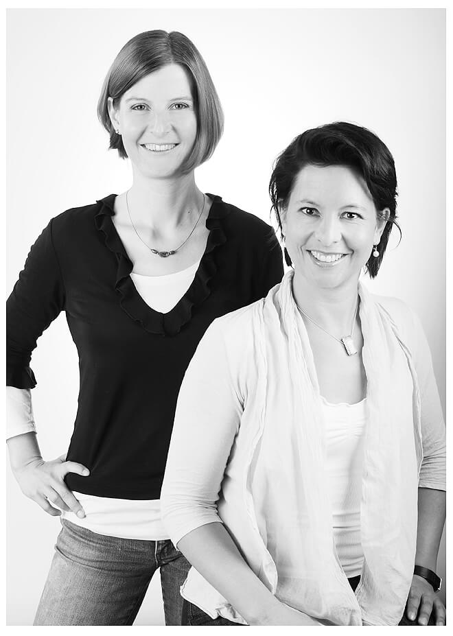 Businessportrait: Zwei Damen in schwarz-weißer Kleidung posieren für ein Foto und strahlen dabei Selbstbewusstsein aus.