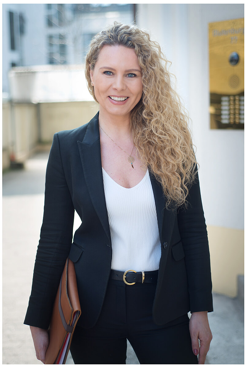 businessportrait_blonde frau_draussen mit mappe in der hand sonnig immobilienkauffrau