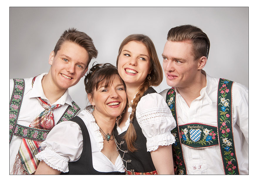 Familienfoto mit Mama und drei erwachsenen Kindern, welches vier Personen in traditioneller bayerischer Kleidung dirndl posieren für ein Foto und Sie tragen Trachtenhüte, Schürzen und Lederhosen