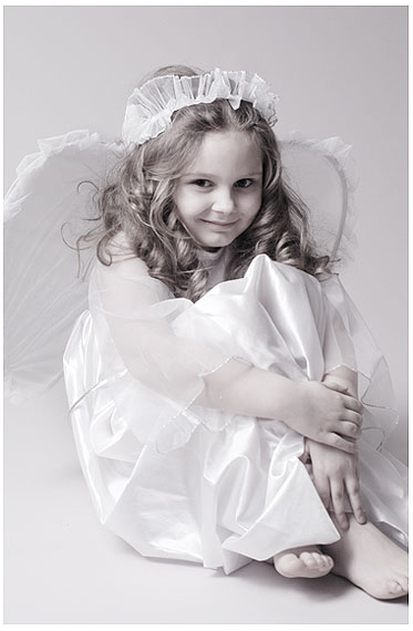 Foto zeigt ein kleines Mädchen in einem weißen Kleid mit Engelsflügeln, das wie ein Engel aussieht
