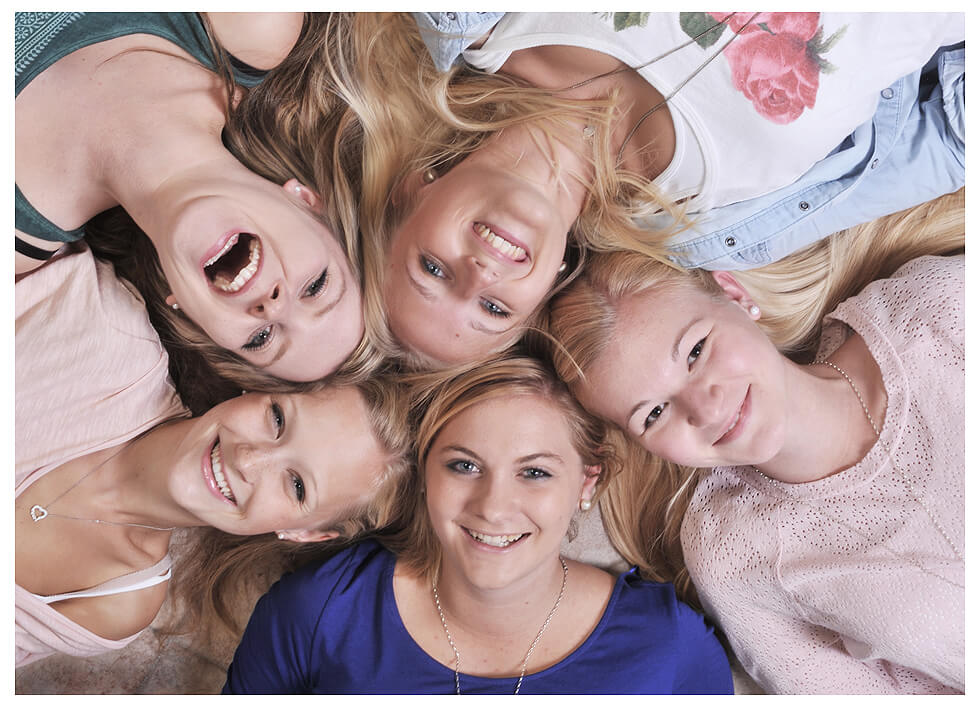 Junggesellenabschied fünf junge Frauen liegen eng aneinander auf dem Boden, ihre Köpfe sind zusammengelegt, während sie lächelnd in die Kamera schauen