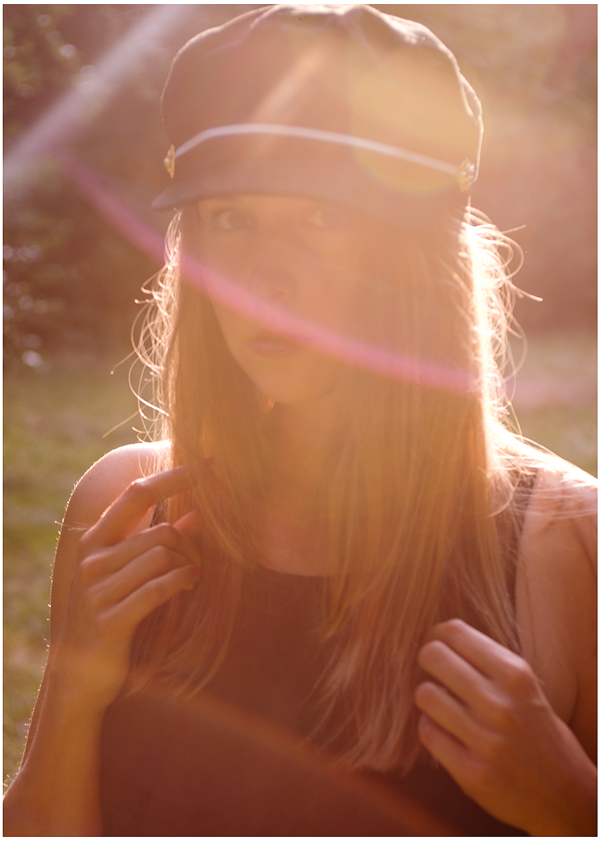Eine Frau genießt die Sonne und schützt sich mit einem Hut, während sie für ein Portrait im Gegenlicht posiert