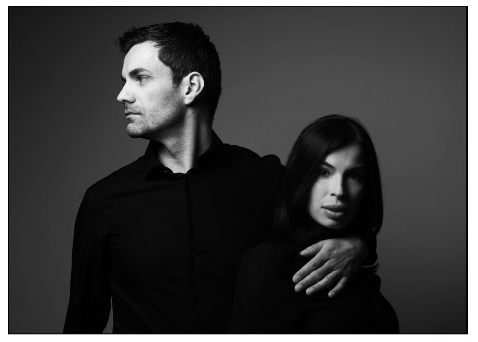 Mann und Frau posieren vor schwarzem Hintergrund für ein Paarshooting, schwarz-weiss