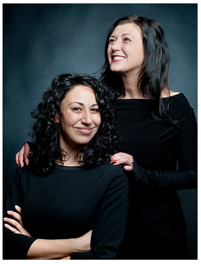 Zwei Freudinnen in eleganten schwarzen Kleidern posieren für ein Foto bei einem Paarshooting, lächelnd