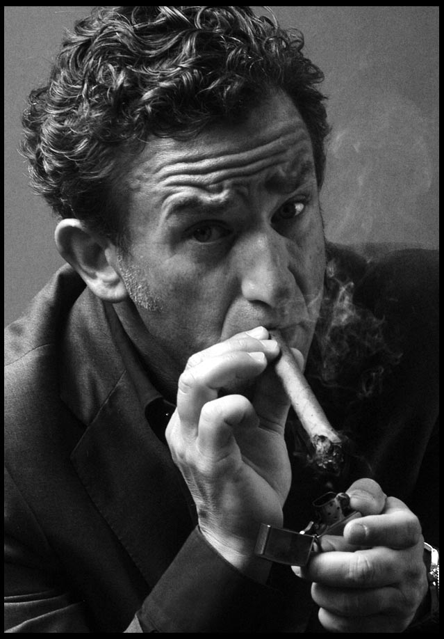 Ein ernst blickender Mann in einem eleganten Anzug raucht genüsslich eine Zigarre. Sein Gesichtsausdruck strahlt Selbstbewusstsein und Autorität aus.