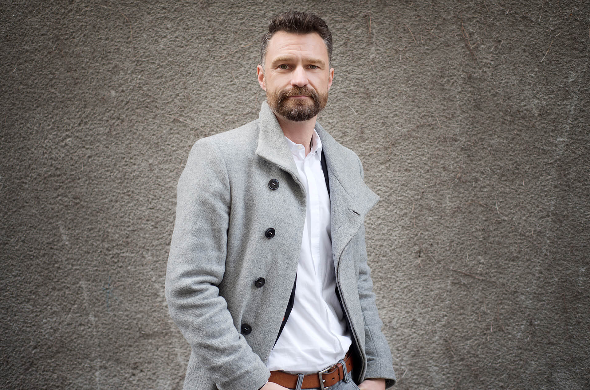 Ein bärtiger Mann in einem grauen Mantel posiert für ein Foto auf Social Media