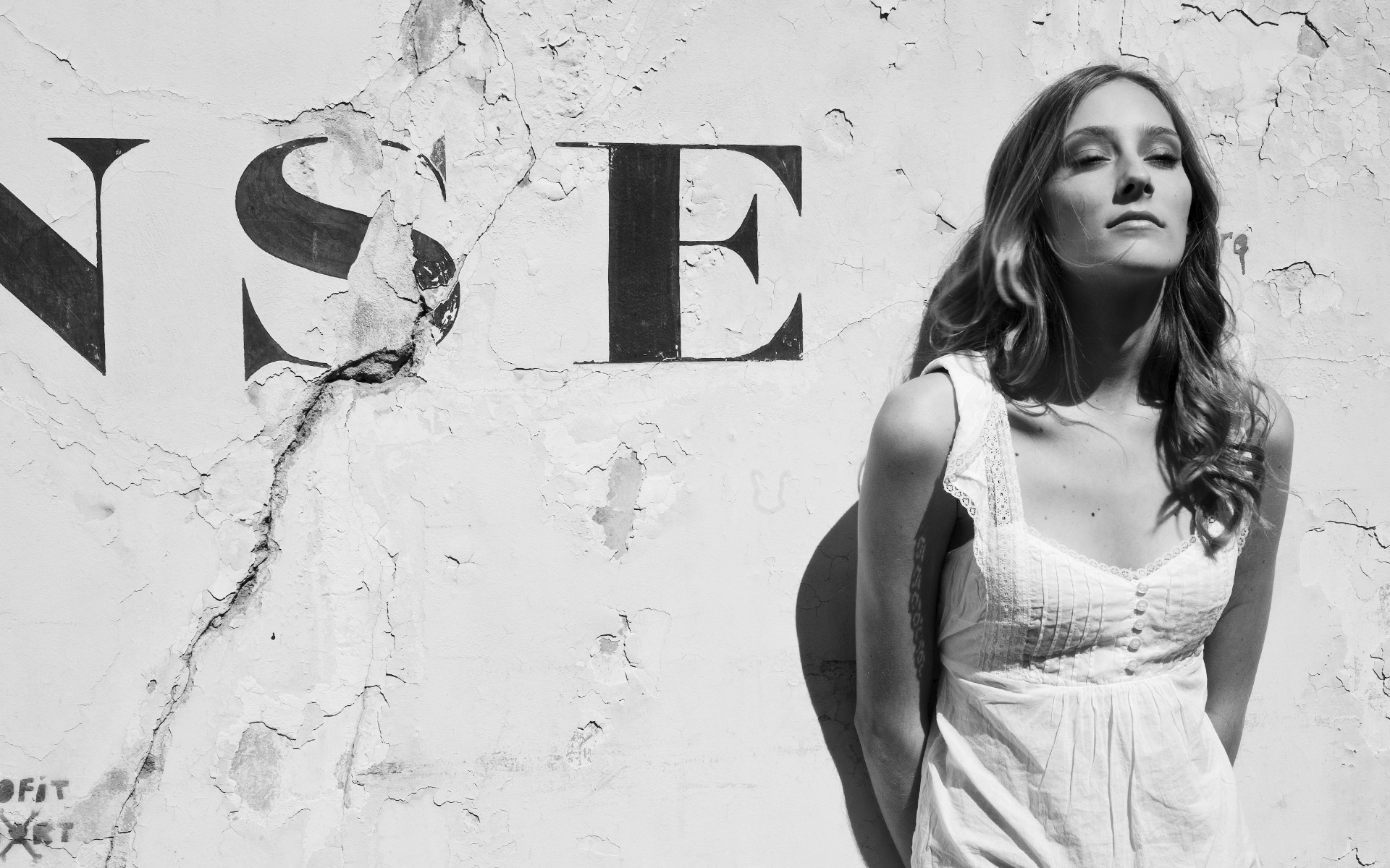 Auf dem Bild ist eine Frau in einem weißen Kleid zu sehen, die neben einer Wand mit der Buchstaben NSE steht. Das Foto wurde für Social Media Zwecke gemacht.