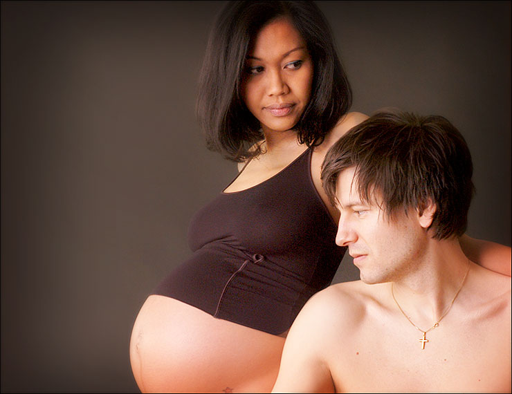 Ein Mann und eine Frau schauen auf den Bauch einer schwangeren Frau Babybauch Fotoshooting