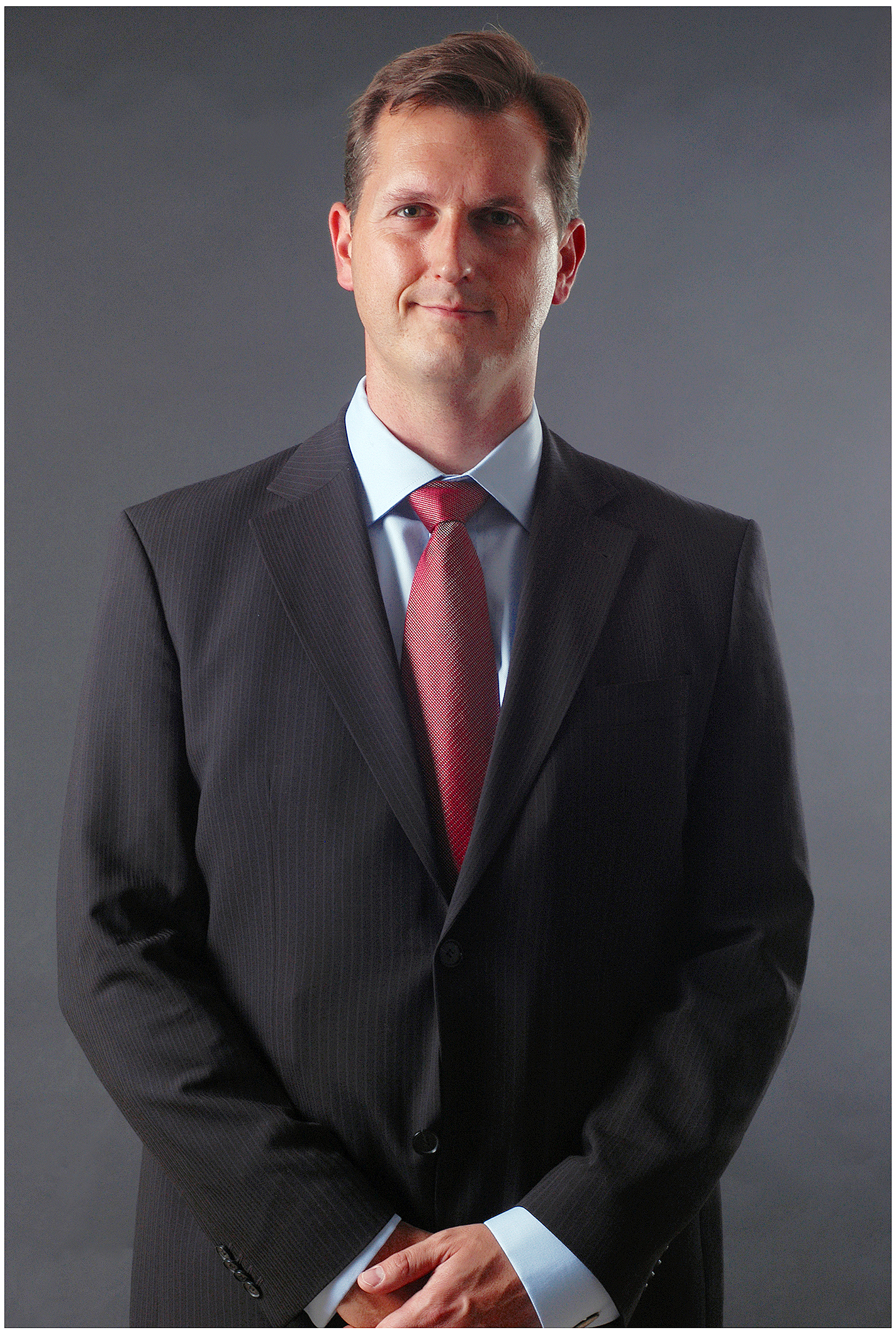 business-portrait-mann-im-anzug-mit-roter-krawatte-stehend-vor-dunklem-hintergrund