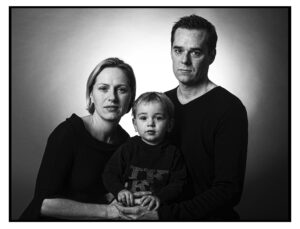 Ein schwarz weißes Bild zeigt einen Mann und eine Frau die ein dreijähriges Kind halten alle schauen ernst in die Kamera