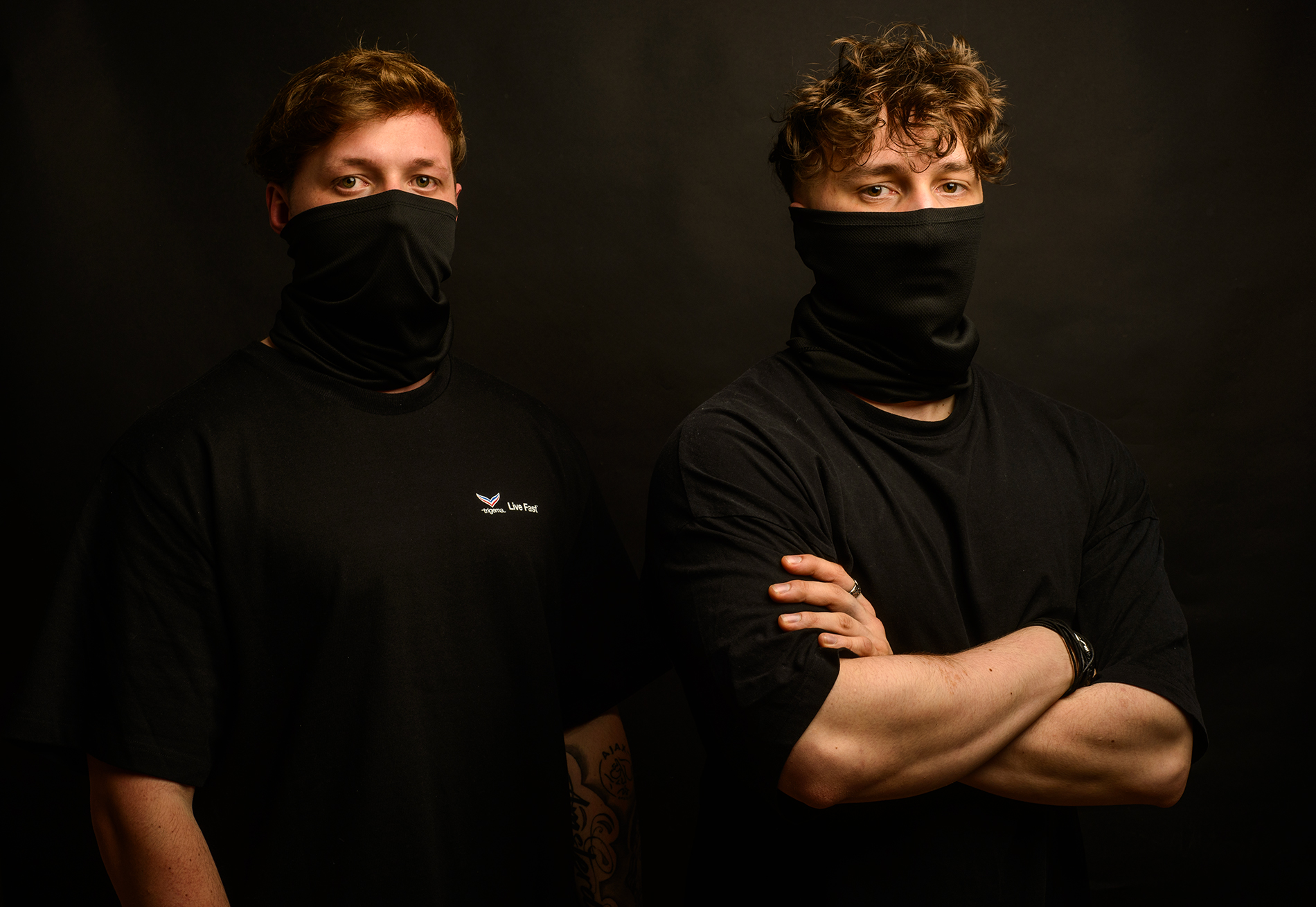 zwei Musiker in schwarzen Masken, Arme verschränkt, im schwarzen Hintergrund