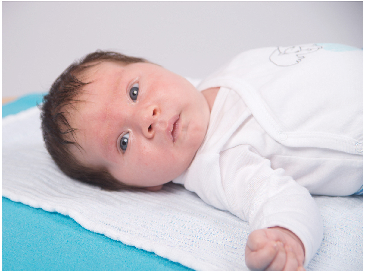Auf dem Bild liegt ein Baby auf einer blauen Decke mit einem weißen Hemd Die blaue Decke bildet einen schönen Kontrast zum weißen Hemd des Babys und verleiht dem Bild eine ruhige und harmonische Stimmung