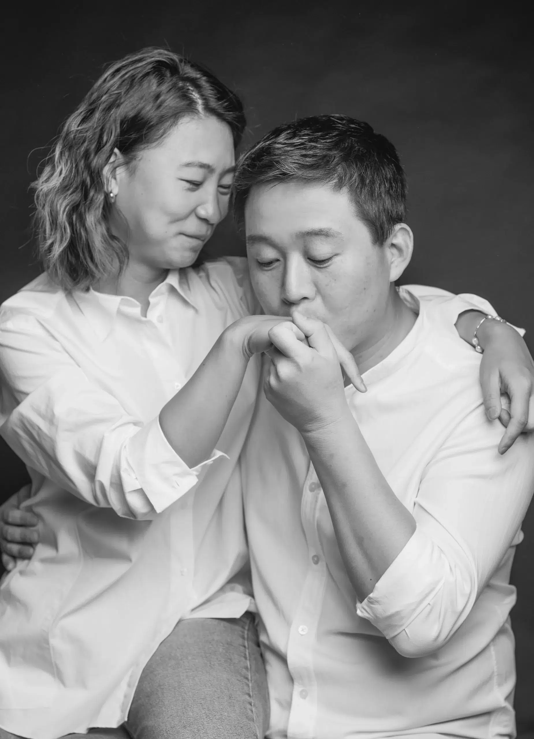 Ein glückliches Paar sitzt und hält liebevoll Hände. Die Frau sitzt auf dem Schoss und beide scheinen entspannt und zufrieden zu sein, der Mann küsst die rechte Hand