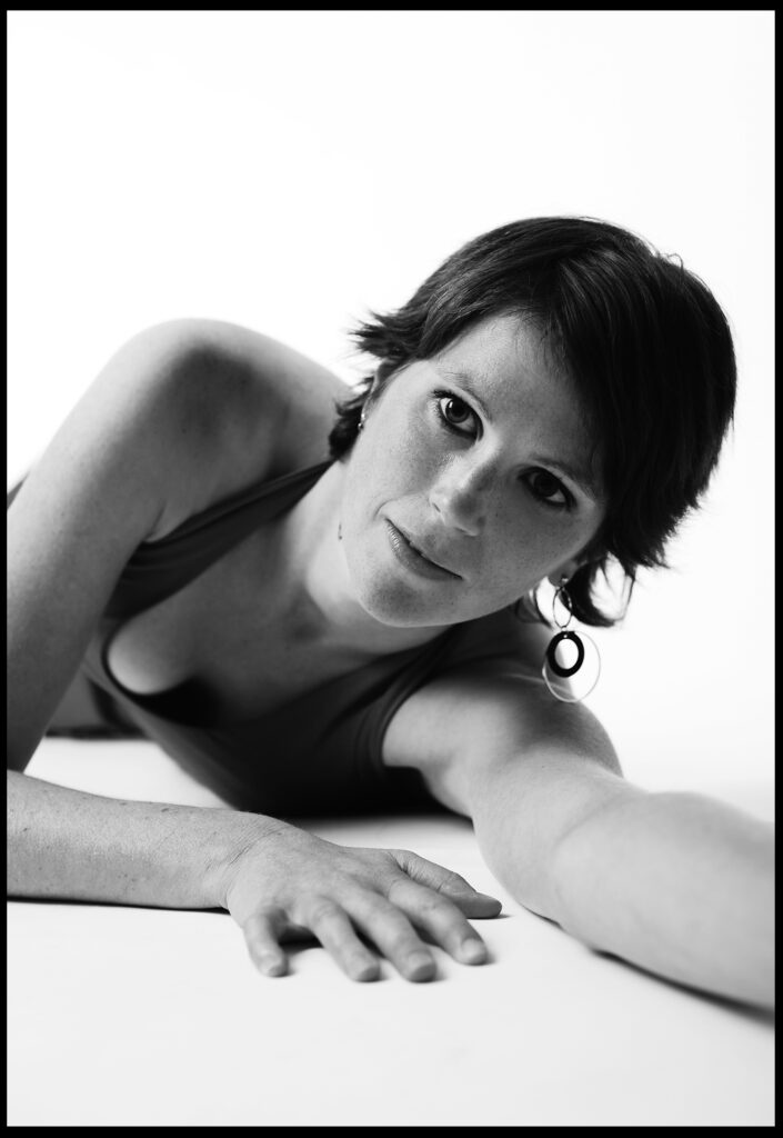 Beauty-Fotoshooting Art vom Fotostudio Belichtungswert München, Schwarzweiß-Portrait einer Frau liegend mit ausgestrecktem Arm, direktem Blick und klarer Bildkomposition