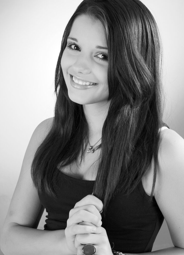 Beauty Fotoshooting im Fotostudio Belichtungswert München, junge Dame mit langem dunklem Haar lächelt natürlich in einem hellen Schwarzweiß-Portrait