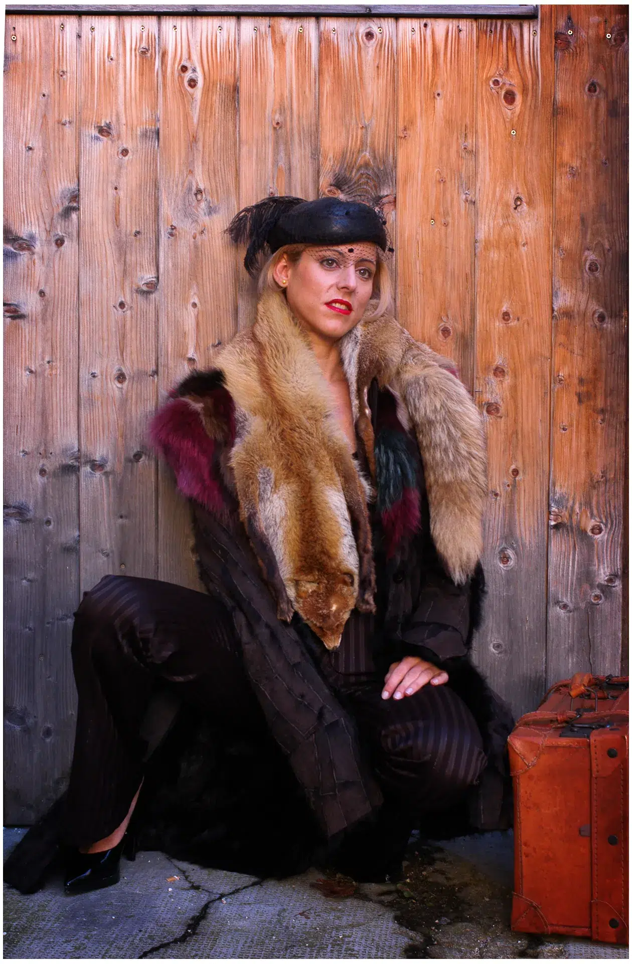ein Model sitzt an einem Holzzaun, gekleidet in einem Pelzmantel und einem Raritäten Hut mit dem Feder 