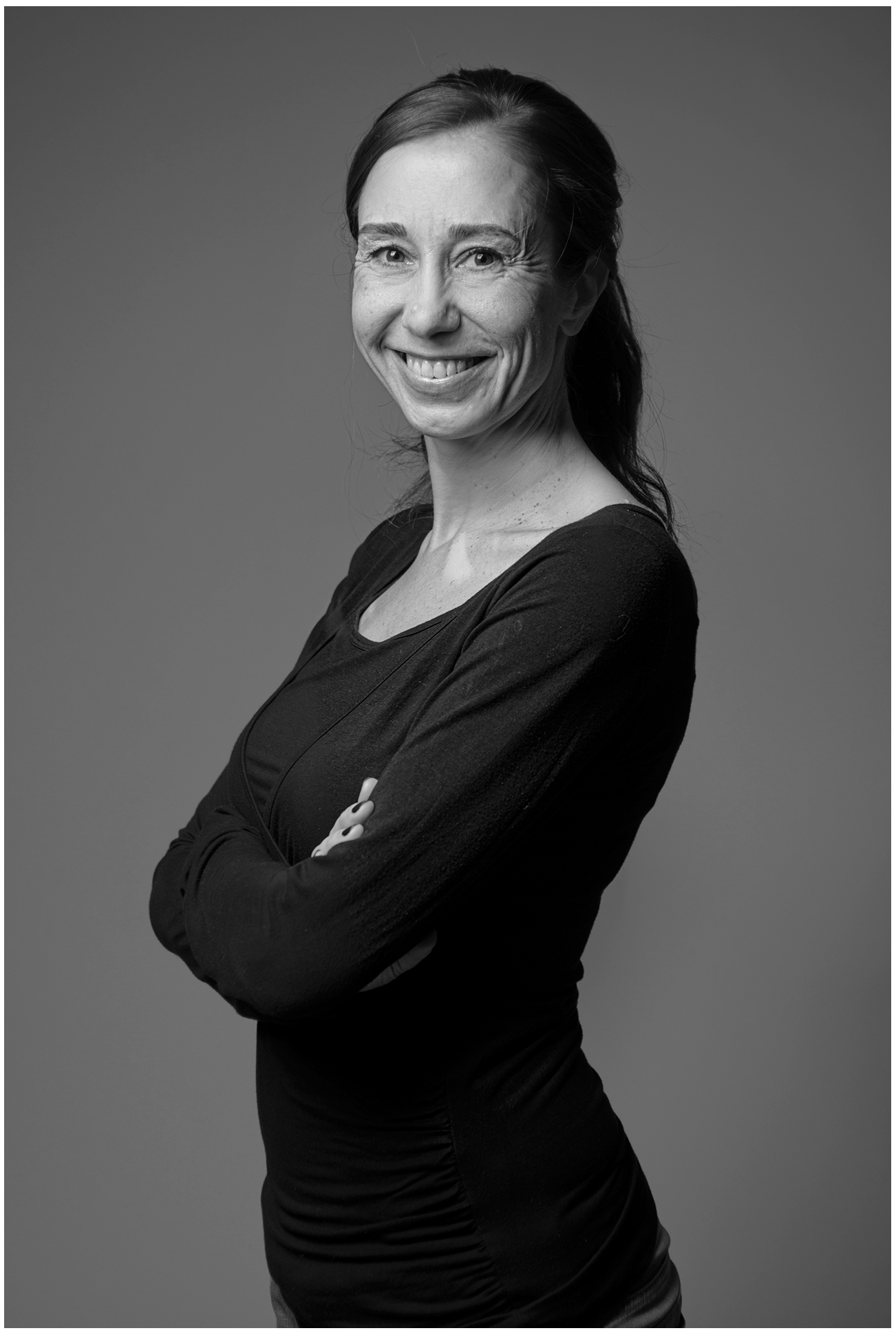 bewerbungsfoto-designerin-portrait-schwarzweiss-profil-armverschaenkt-grauer-hintergrund-studio