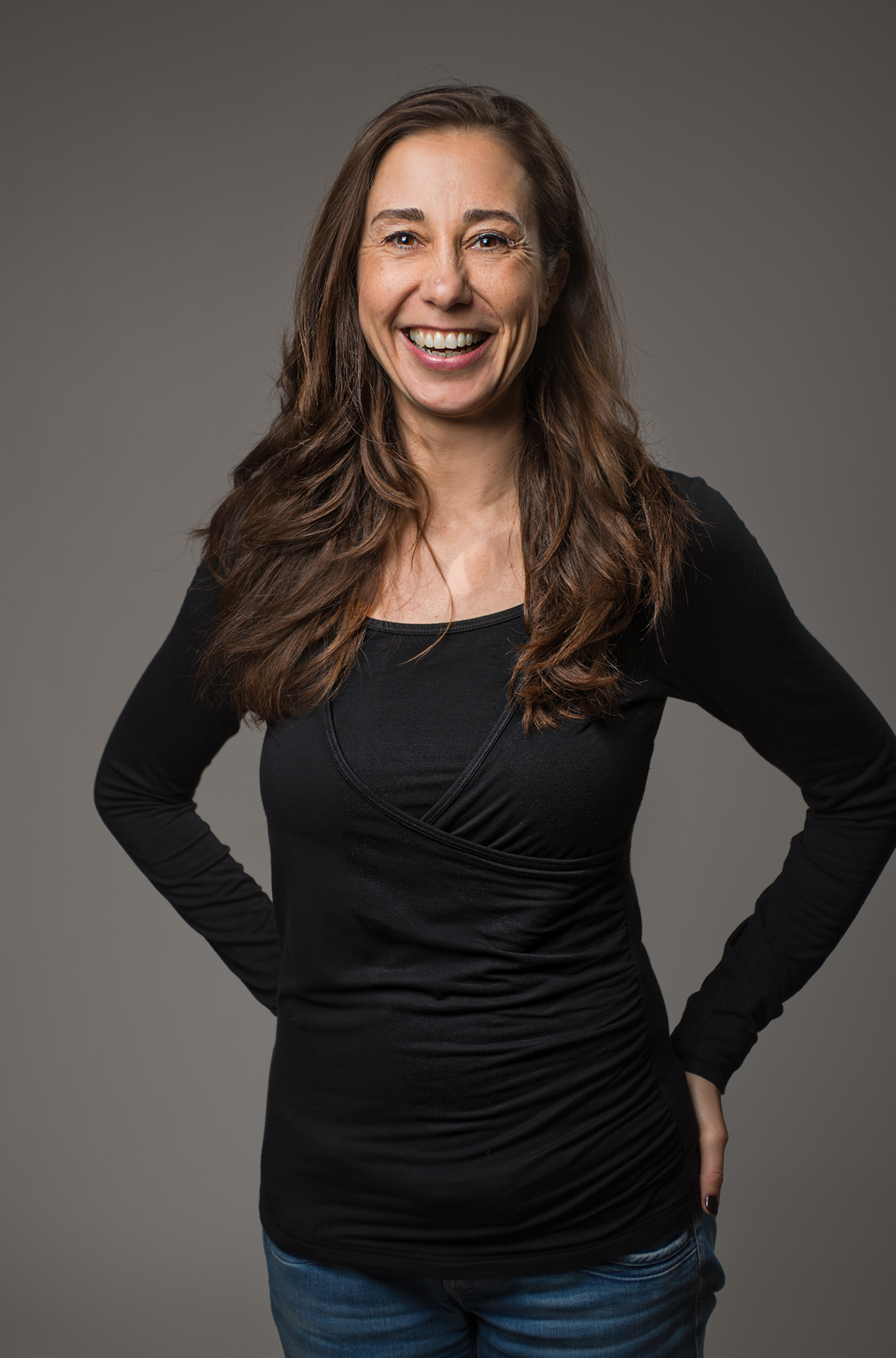bewerbungsfoto-designerin-kreativer-bereich-portrait-stehend-schwarzes-top-jeans-grauer-hintergrund-fotostudio