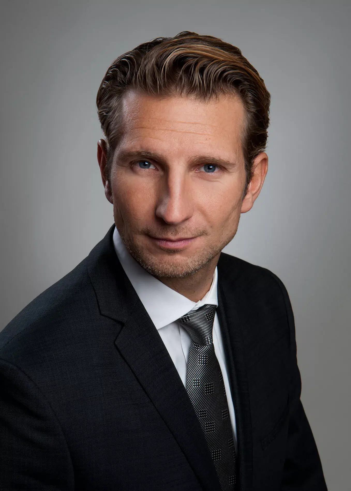 Ein Mann in Anzug und Krawatte posiert für ein Foto. Seine Kleidung ist elegant, seine Pose ist selbstbewusst und sein Blick ist fokussiert.

