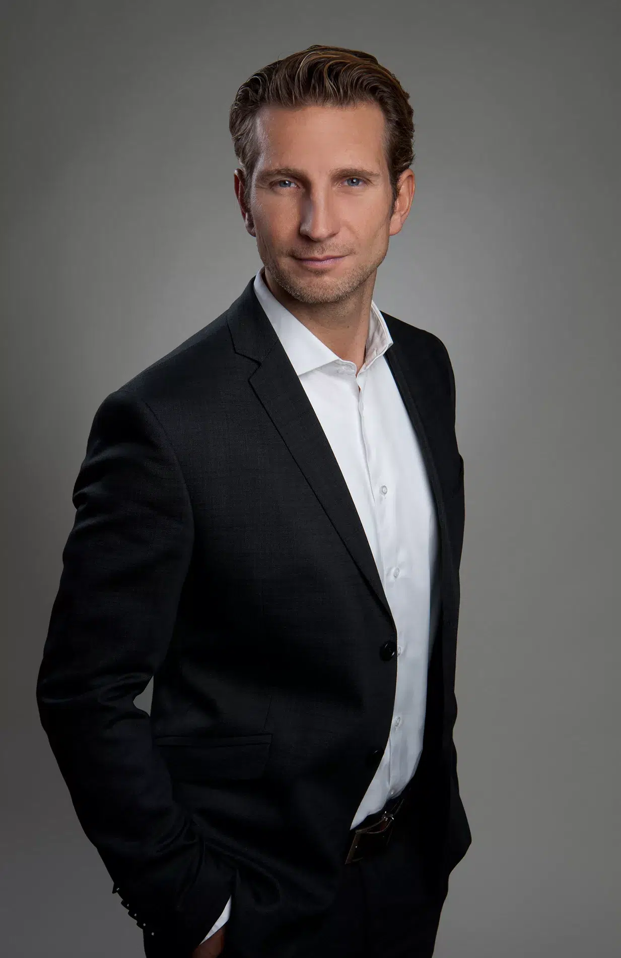 Ein Mann in Anzug posiert für ein Foto. Seine Kleidung, Pose und Blick sind auffällig.