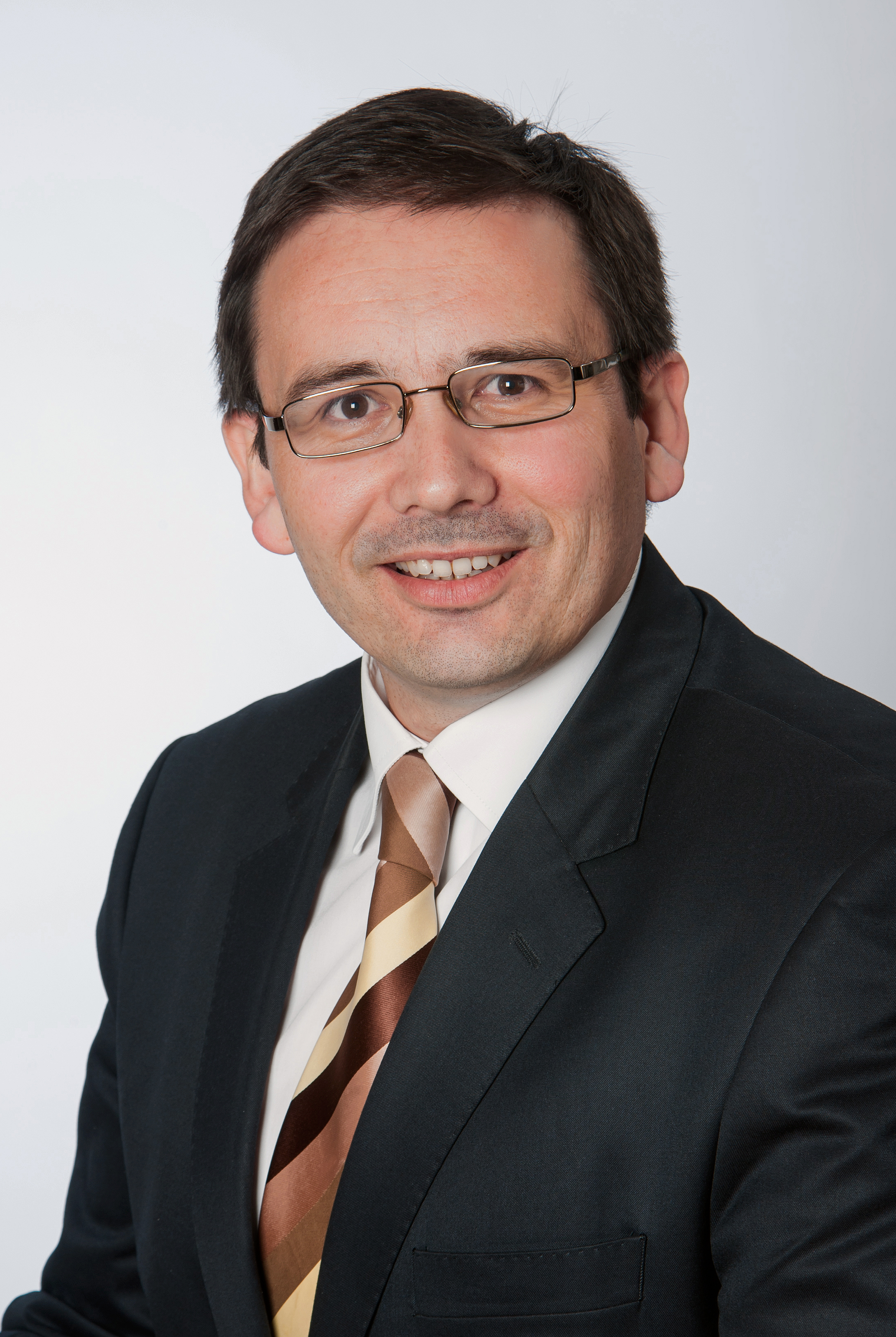 klassisches-business-headshot-mann-mit-brille-im-anzug-und-krawatte-laechelnd-heller-neutraler-hintergrund