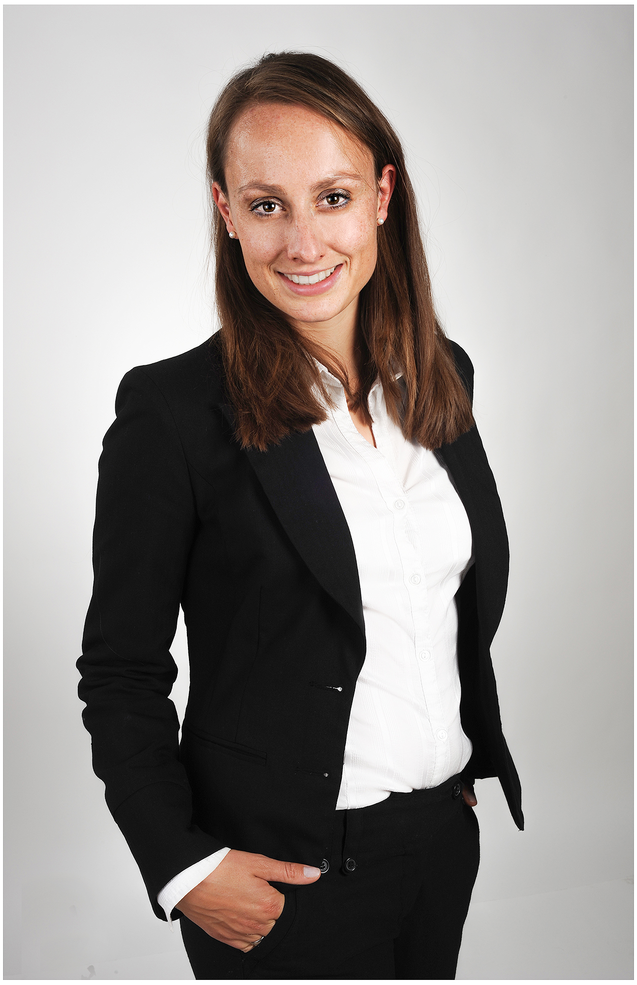 professionelles-businessportrait-im-studio-frau-im-schwarzen-hosenanzug-und-weisser-bluse-lockere-haltung-freundliches-lächeln-neutraler-hintergrund