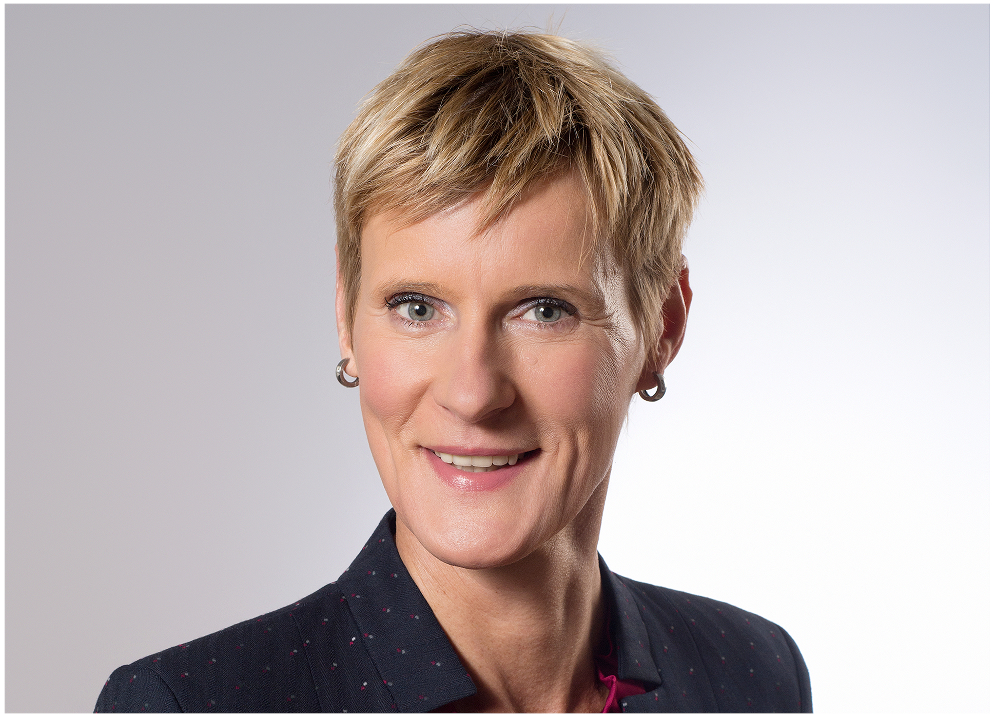 professionelles-businessportrait-im-fotostudio-frau-mit-kurzhaarschnitt-im-dunklen-blazer-und-bordeaux-bluse-laechelt-vor-neutralem-hintergrund