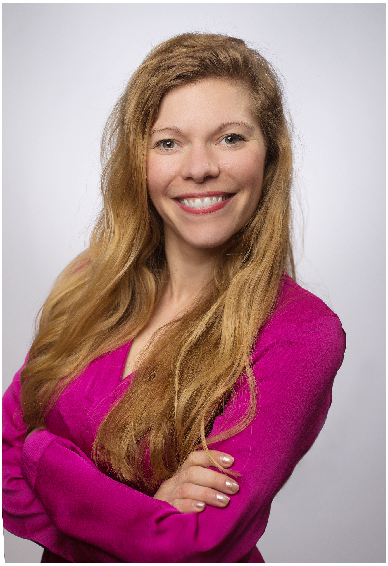 Freundliches Businessportrait einer blonden Frau mit verschraenkten Armen und Laecheln im Studio Businessfotografie fuer Unternehmen in Muenchen