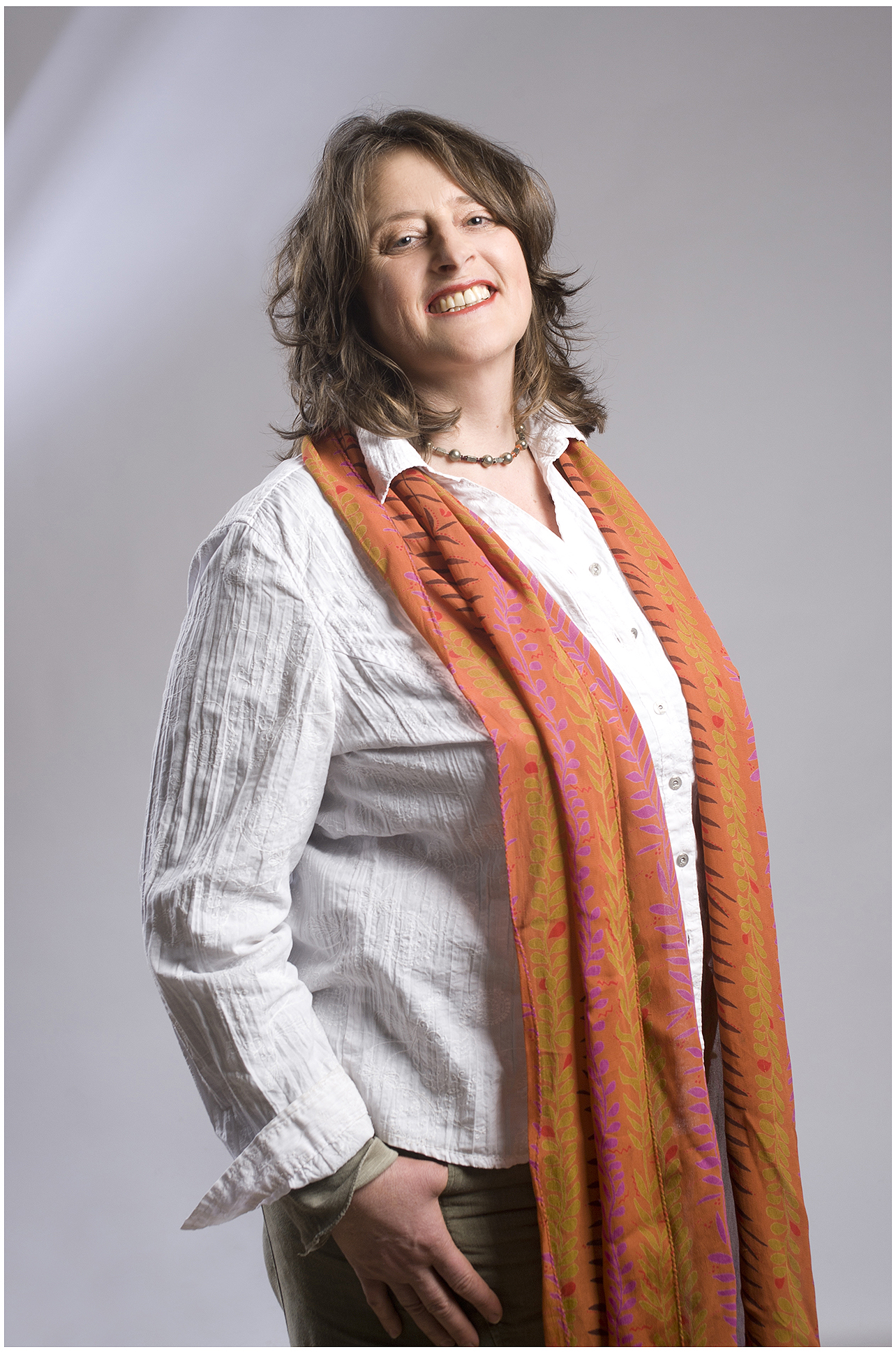 Businessportrait einer Coachin und Mentorin: weiße Bluse, orangefarbener Schal, freundliches Lächeln vor grauem Hintergrund – Personal Branding Fotografie München