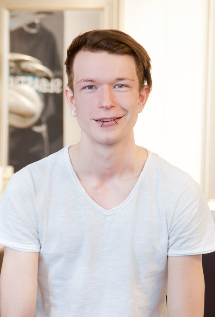 Businessportrait eines jungen Friseurs im Salon: natürlicher Look, freundlicher Blick, weiches Hintergrundbokeh – Mitarbeiterportraits München