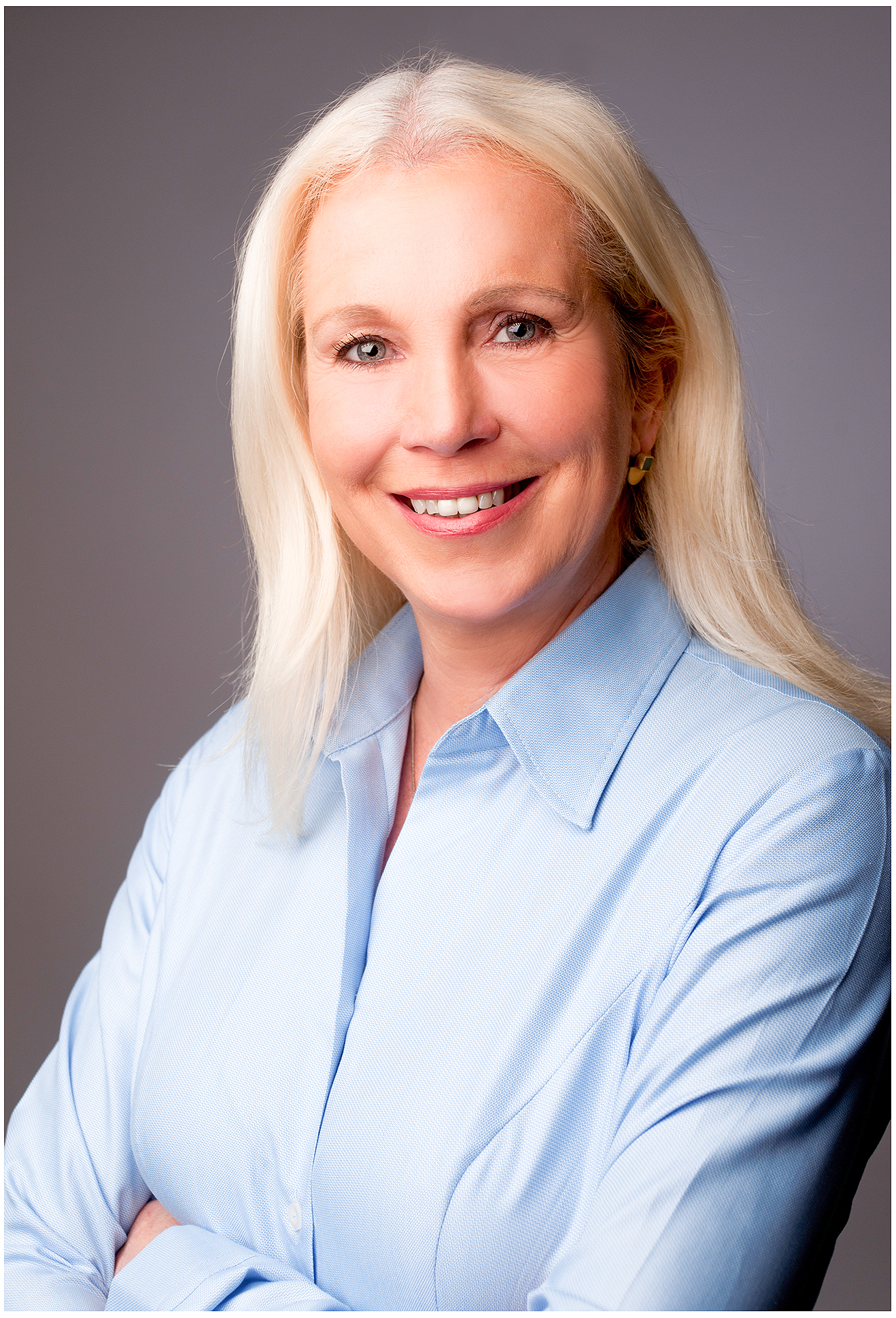 Nahes Businessportrait einer Geschäftsführerin im Finanzbereich mit hellblauem Hemd, grauer Hintergrund, sympathischer Blick