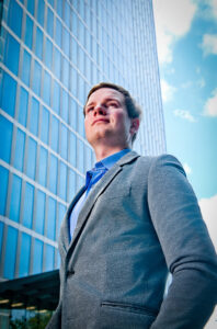 Hochwertiges Unternehmensportrait im urbanen Umfeld, Mann im Anzug vor moderner Glasarchitektur, fotografiert von Belichtungswert München