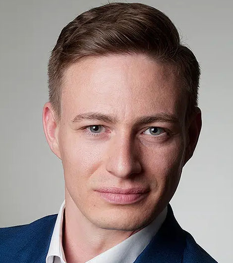 Businessportrait vom Fotostudio Belichtungswert München, professionelles Bewerbungsfoto eines jungen Mannes im blauen Sakko und weißen Hemd, frontal aufgenommen vor hellgrauem Studiohintergrund mit ruhigem, selbstbewusstem Blick in die Kamera.