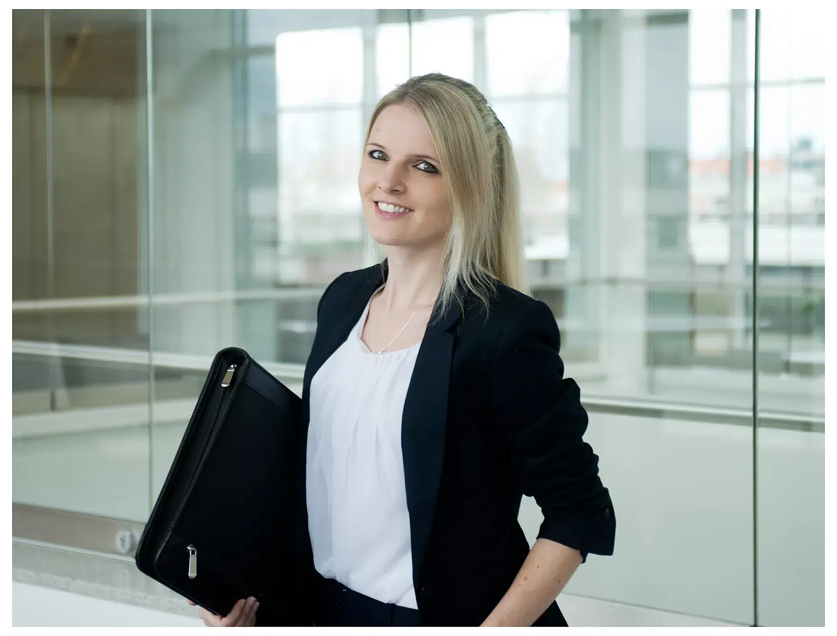 Junge Beamtin mit einer Mappe in einem Glasgebäude, Businessportrait