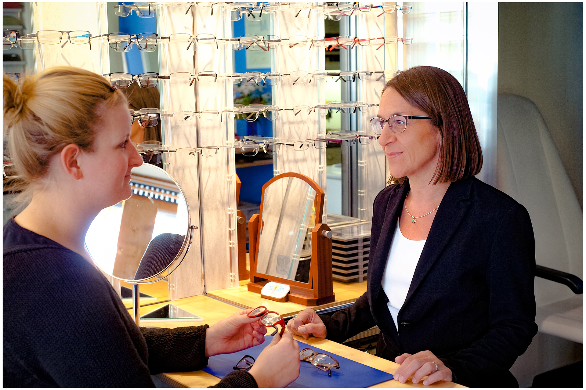 Businessreportage im Optikergeschäft: Optikerin berät Kundin bei der Brillenauswahl am Tisch – Firmenfotografie im Raum München