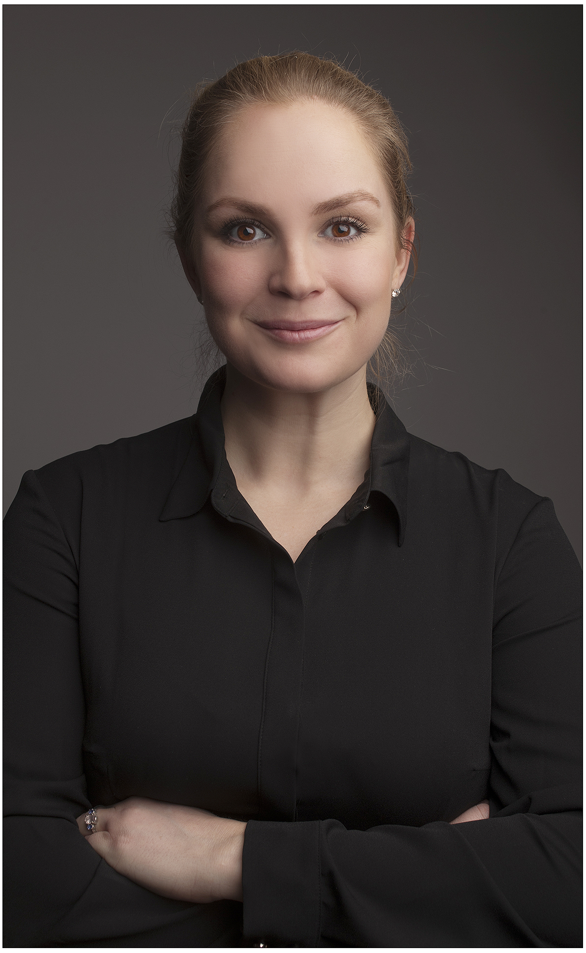 professionelles-executive-headshot-im-studio-blonde-frau-in-schwarzer-bluse-souveraener-ausdruck-dunkler-hintergrund-weiches-licht