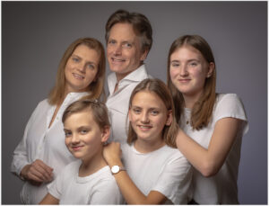 Familienfoto im Fotostudio Belichtungswert München mit Eltern und drei Kindern in heller Kleidung vor grauem Hintergrund