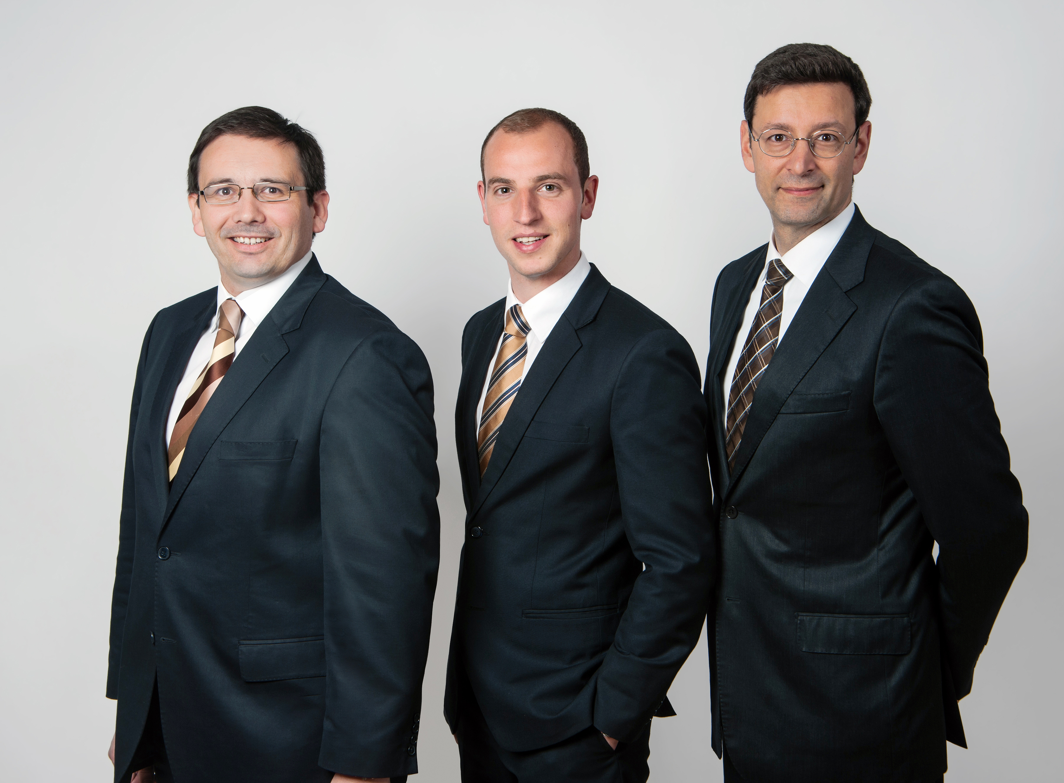 firmenshooting-gruppenfoto-drei-kollegen-im-anzug-mit-krawatte-professionell-laechelnd-heller-neutraler-hintergrund