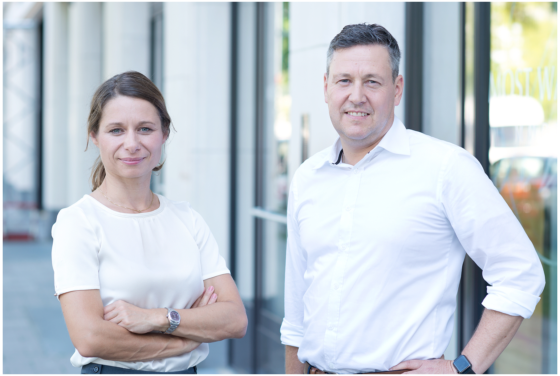 Firmenshooting vom Fotostudio Belichtungswert München, Businessportrait von Mann und Frau in weißer Businesskleidung vor moderner Firmenfassade outdoor