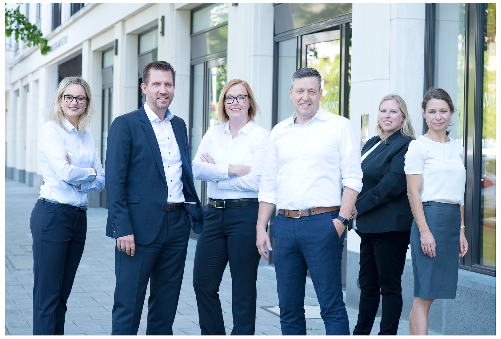 Firmenshooting vom Fotostudio Belichtungswert München, sechs Mitarbeiter stehen als seriöses Business-Team outdoor vor einer modernen Glasfassade