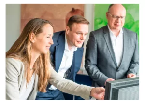 eine Gesprächssituation im Büro - Frau zeigt auf den Bildschirm und erklärt zwei anderen Mitarbeiter