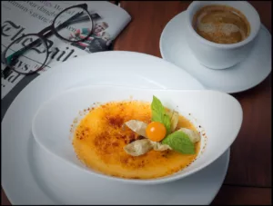 Passionsfrucht Creme Brûlée auf dem Tisch als Stillleben mit Brille Zeitung und Kaffee