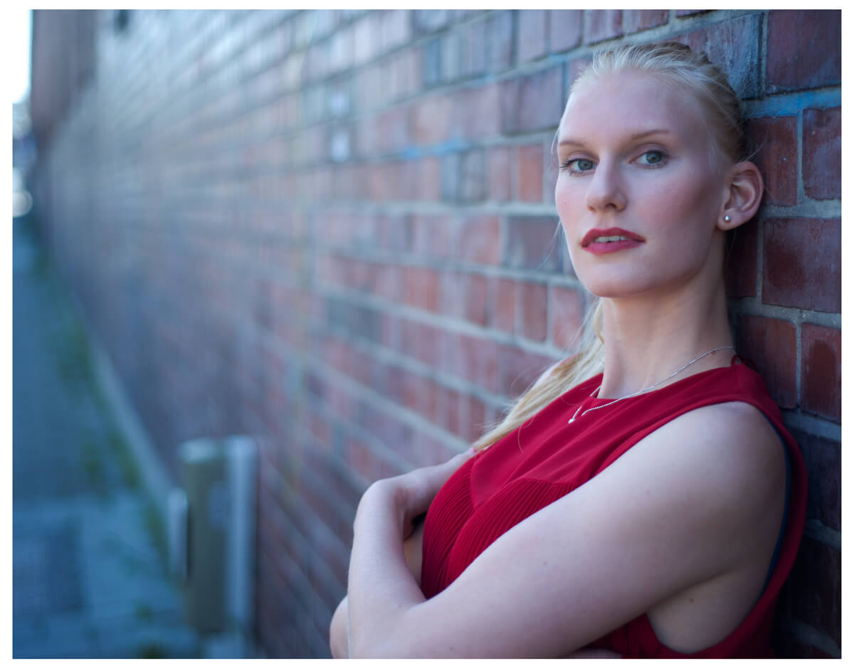 Fotograf in München fotografiert ein blondes Model an der alten Wand, im Roten Oberteil, Haende verschraenkt, 