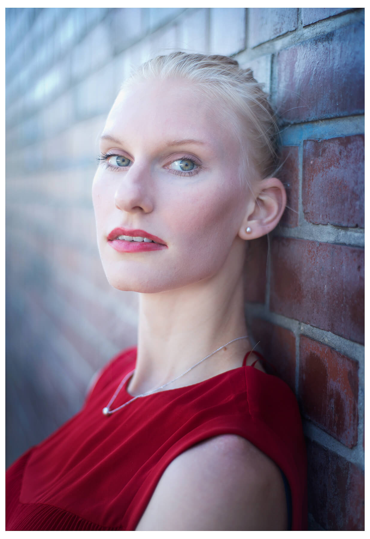 Fotograf in München fotografiert ein blondes Model an der Wand, im Roten Oberteil, stehend