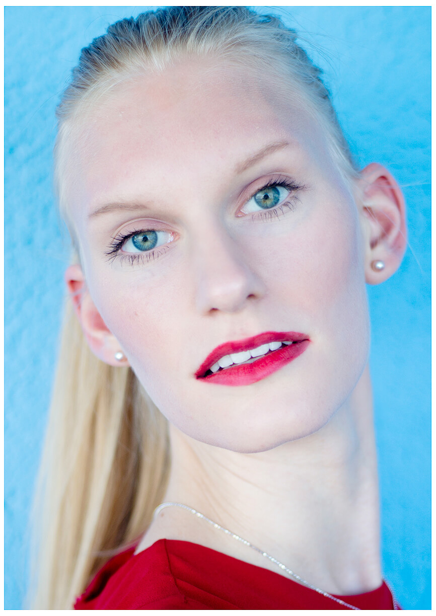 Fotograf in München fotografiert ein blondes Model an der blauen Wand, im Roten Oberteil, close up, Portrait
