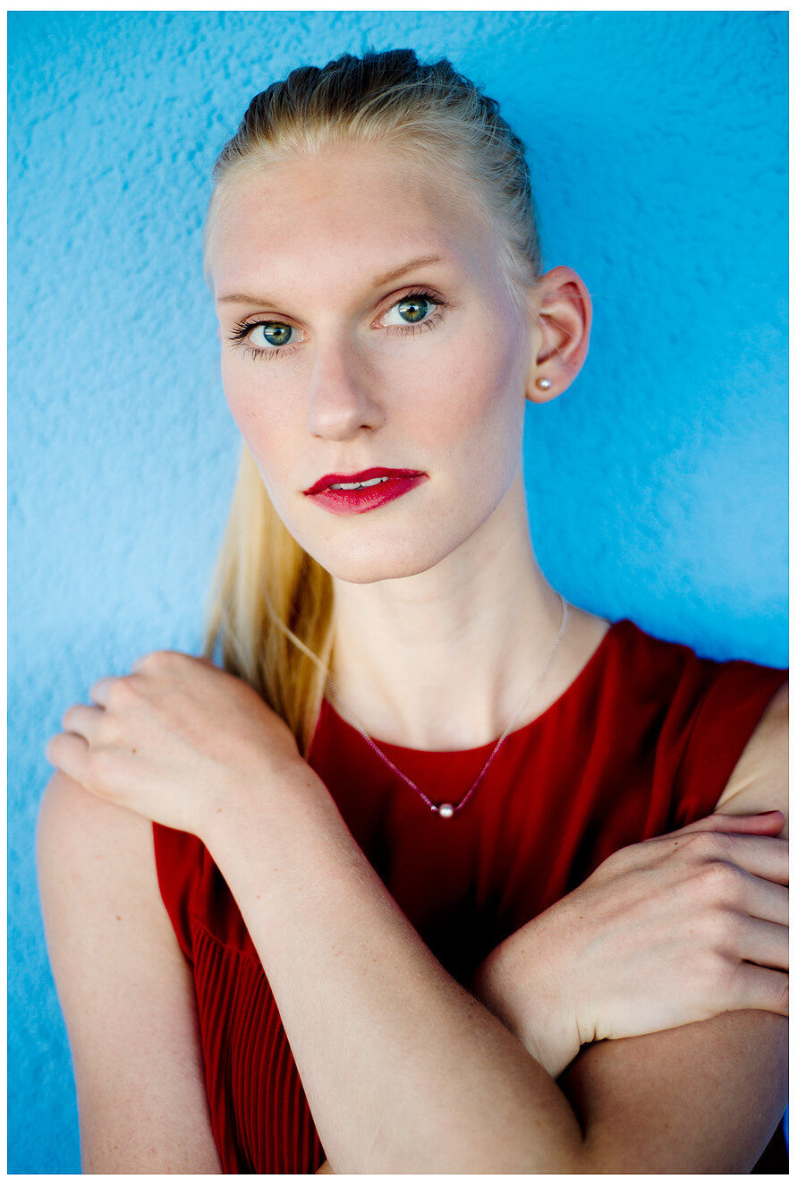 Fotograf in München fotografiert ein blondes Model an der blauen Wand, im Roten Oberteil, stehend