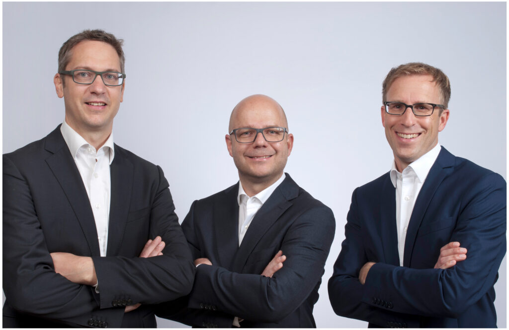 Professionelles Gruppenportrait von drei Geschäftsleuten in dunklen Anzügen beim Firmenshooting im Fotostudio Belichtungswert in München.